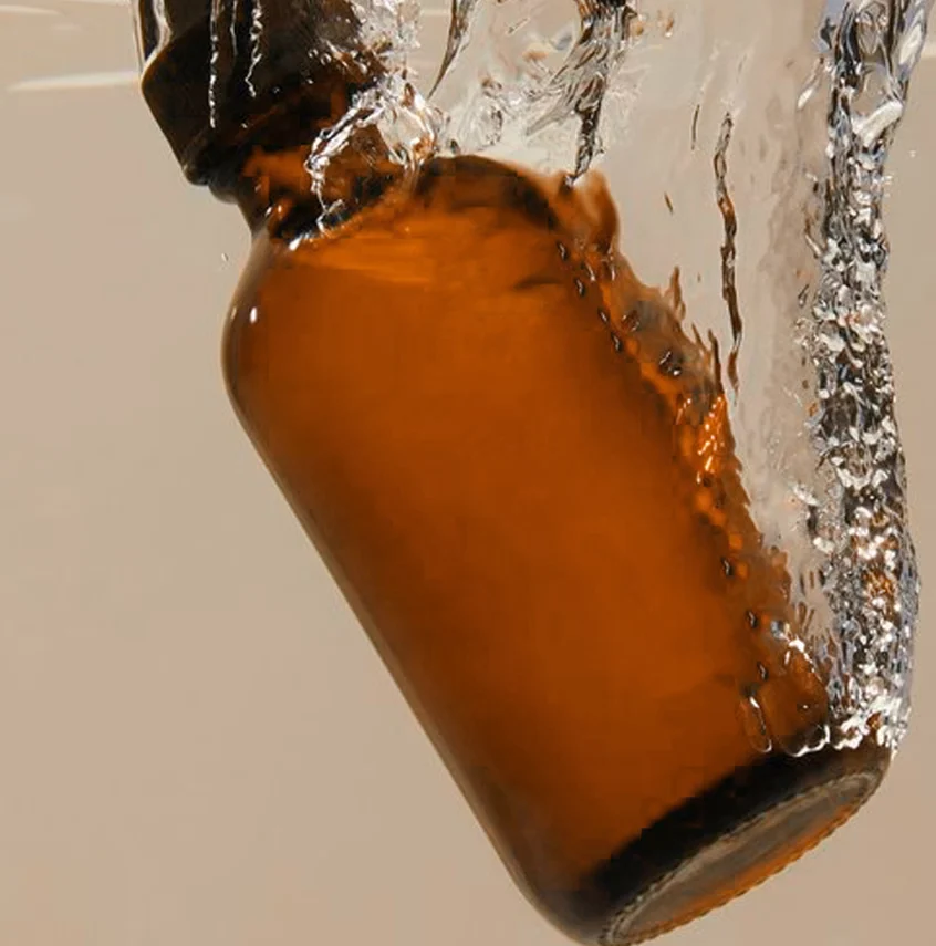 An amber skincare bottle splashing into water